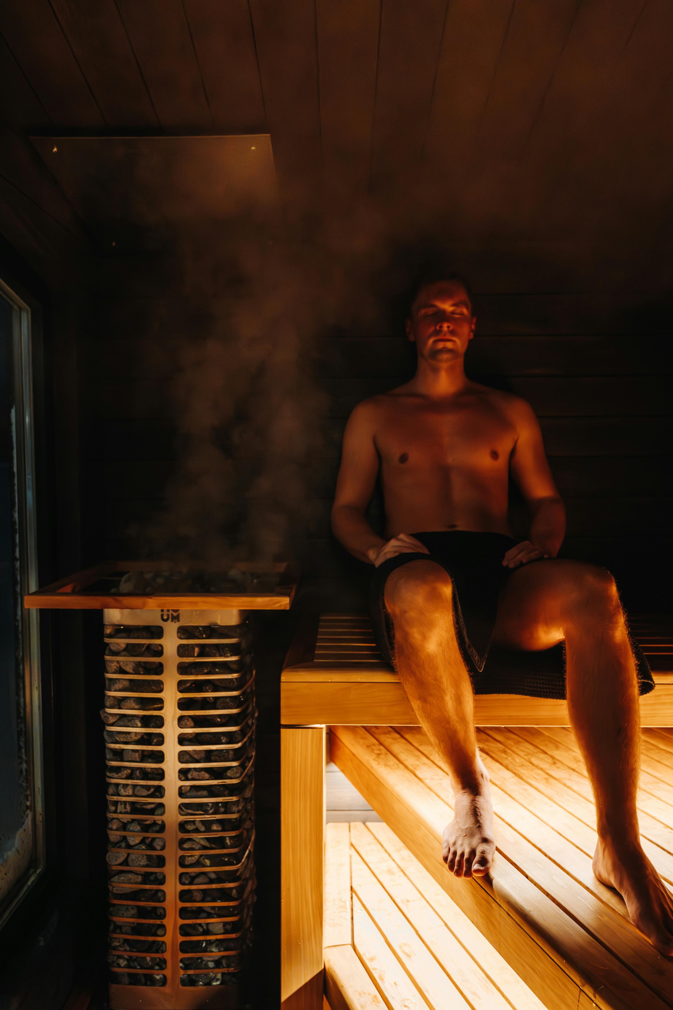 En mand sidder i en sauna ved en dampende saunaovn