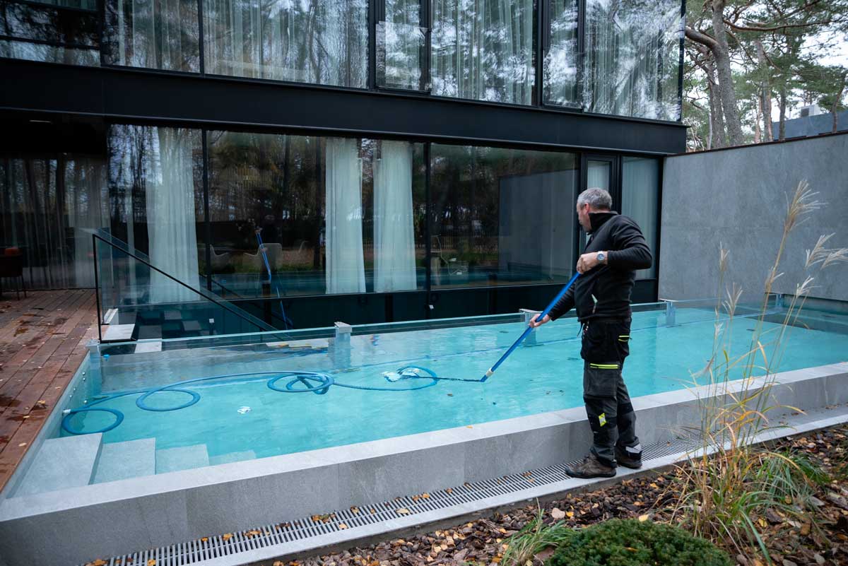 Udendørs swimmingpool med uklart og snavset vand, brune pletter og snavs synligt på overfladen, en person stående ved siden af poolen