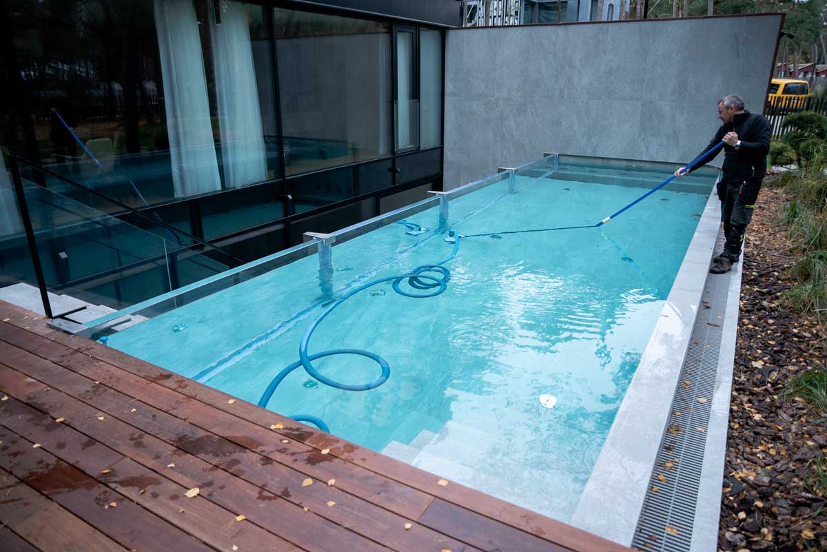 En swimmingpool med lysegrønt og uklart vand, overfladen dækket af et lag alger, en situation fanget hvor en person rengør poolen.